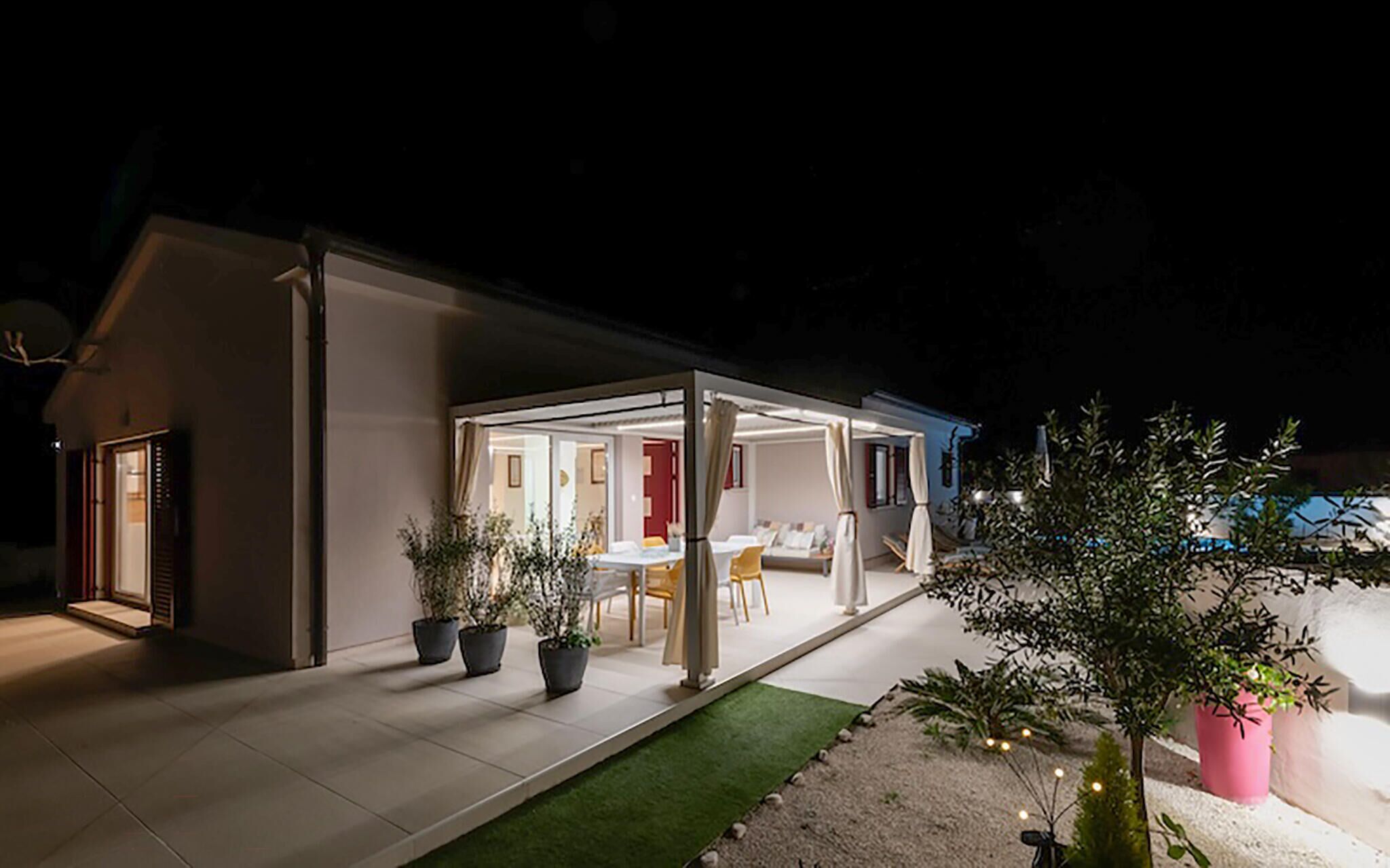 Une maison moderne dotée d’un patio couvert, d’une table à manger et de plusieurs plantes en pot.