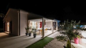 Une maison moderne dotée d’un patio couvert, d’une table à manger et de plusieurs plantes en pot.