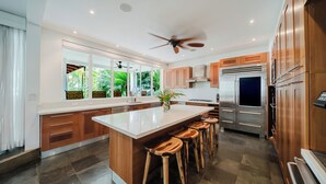 Cozinha moderna com uma ilha grande, banquetas de madeira, eletrodomésticos de aço inoxidável e vista para o verde lá fora.