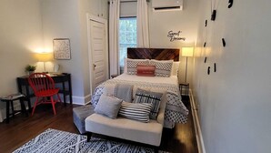 Een slaapkamer met een bed, nachtkastje, stoel en een muur met een bord.