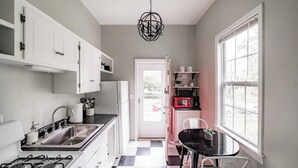 Een moderne keuken met witte kasten, een zwart-wit geruit vloertje, een eethoek met een zwarte tafel en witte stoelen, en een rode magnetron op een plank.