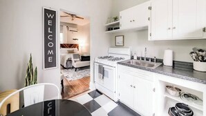 Een moderne keuken met witte kasten, een fornuis en een spoelbak. Er hangt een welkomstbord aan de muur en er is een plafondventilator in de eethoek.