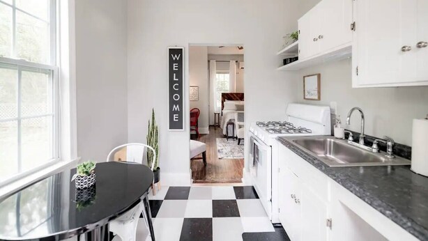 Een moderne keuken met witte kastjes, een zwart-wit geruite vloer en een welkomstbord.