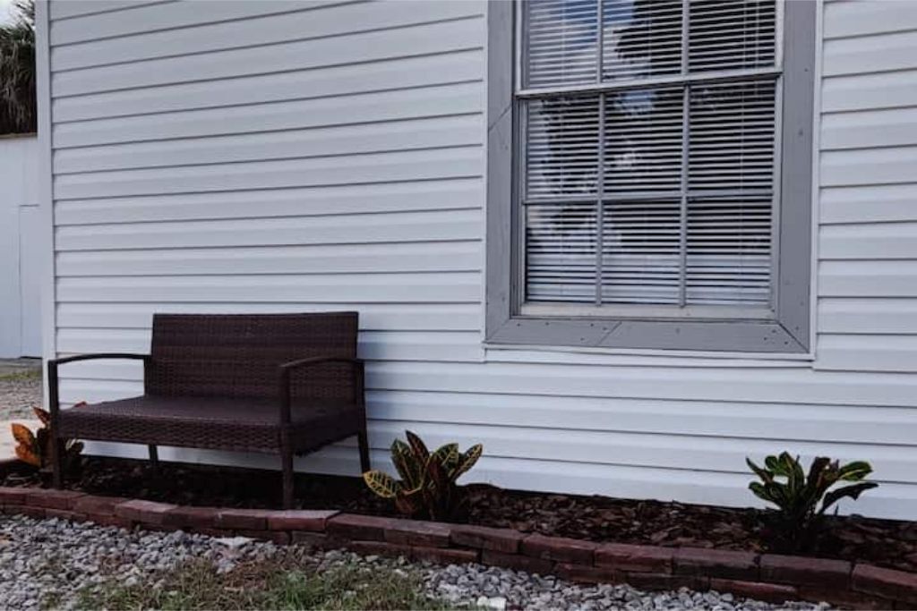 A bench outside a house with a window.