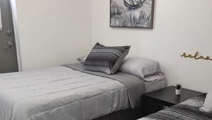 Un dormitorio con dos camas, una mesita de noche con una planta, un cuadro en la pared y un cartel que dice 'relax'.