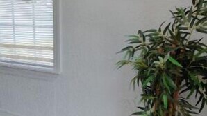 Una habitación con un ventanal grande, un tablón de anuncios con folletos de viaje y una planta en maceta.