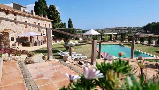 A pool area with lounge chairs and umbrellas, a stone building, and a view of the countryside. - Spacious apartment in Historical Country Estate (Teulada)
