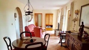 A dining area with a round table and chairs, a kitchen in the background, and a living area with a sofa and curtains. - Spacious apartment in Historical Country Estate (Teulada)