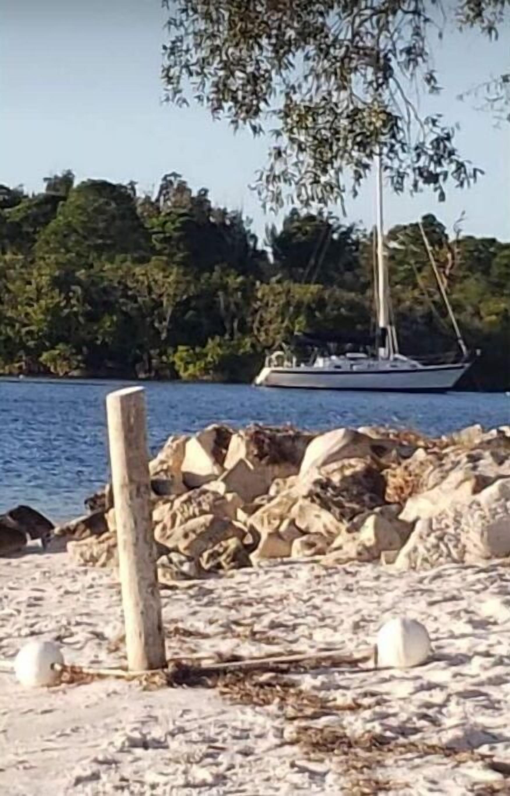 Una playa con rocas y un velero en el agua.