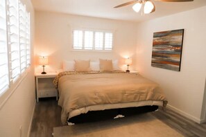 Quarto com cama, duas mesas de cabeceira com luminárias, janela e um quadro na parede.