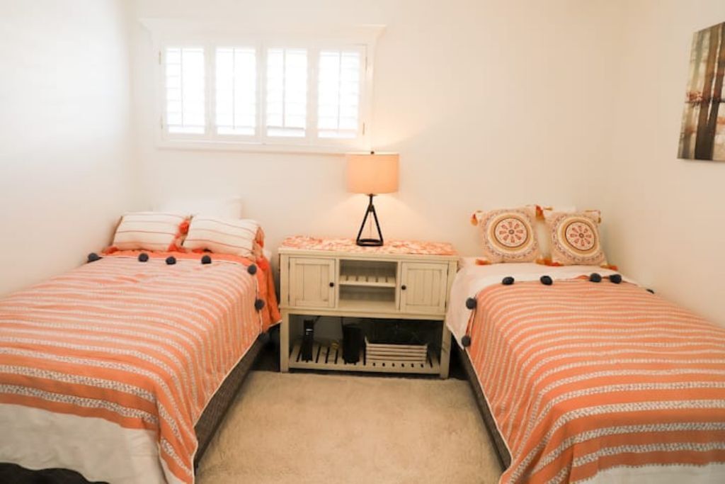 A bedroom with two beds, a nightstand, a lamp, and a window.