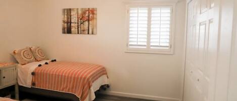 A bedroom with a bed, a nightstand, a ceiling fan, a window with blinds, and a door.