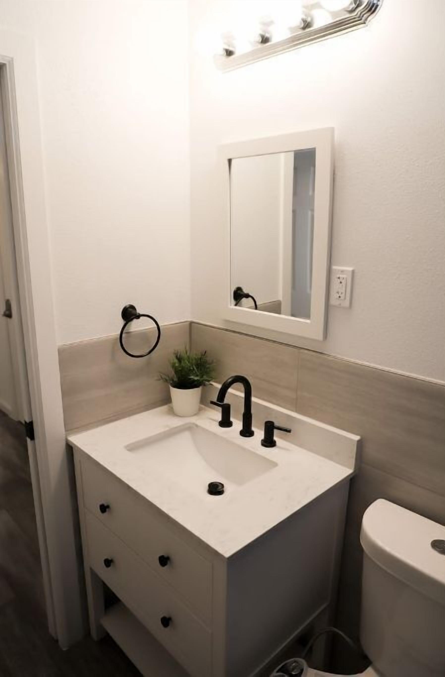 Une salle de bain avec un lavabo blanc, un robinet noir et un miroir au-dessus.