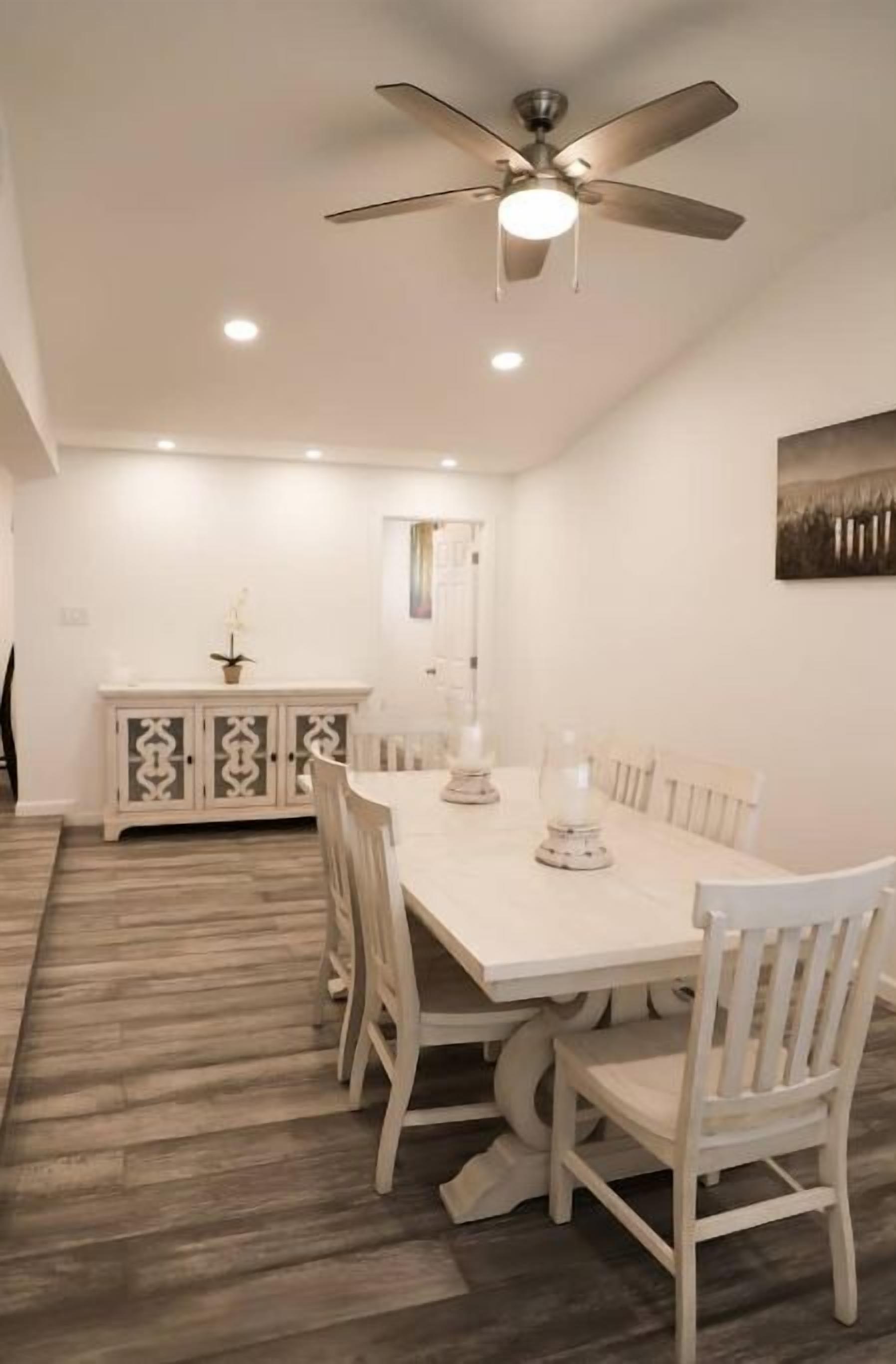 A dining area with a white table, white chairs, a ceiling fan, and a cabinet with decorative patterns.