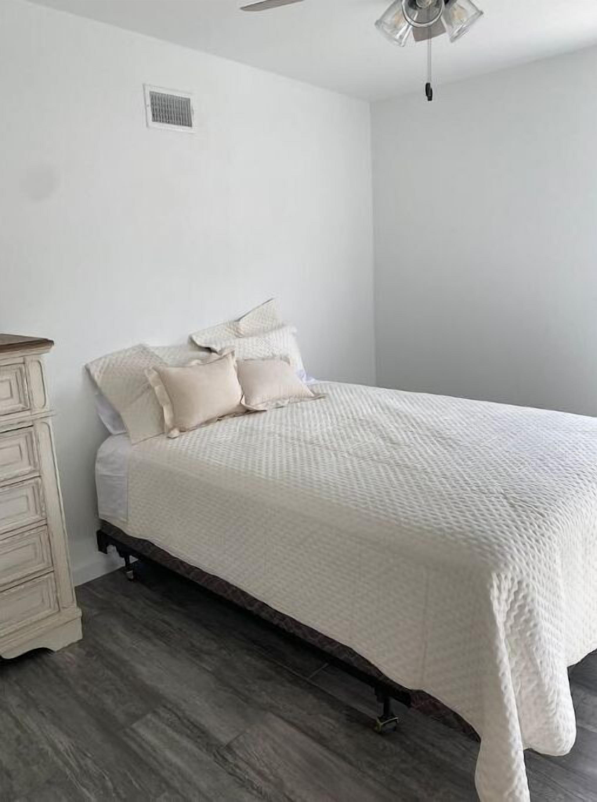 A bedroom with a bed, a dresser, and a ceiling fan.