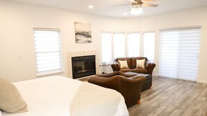A spacious bedroom with a large bed, a leather armchair, and a fireplace.