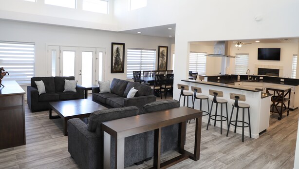 A spacious living area with a dark gray sectional sofa, a wooden coffee table, and a kitchen with a bar area.