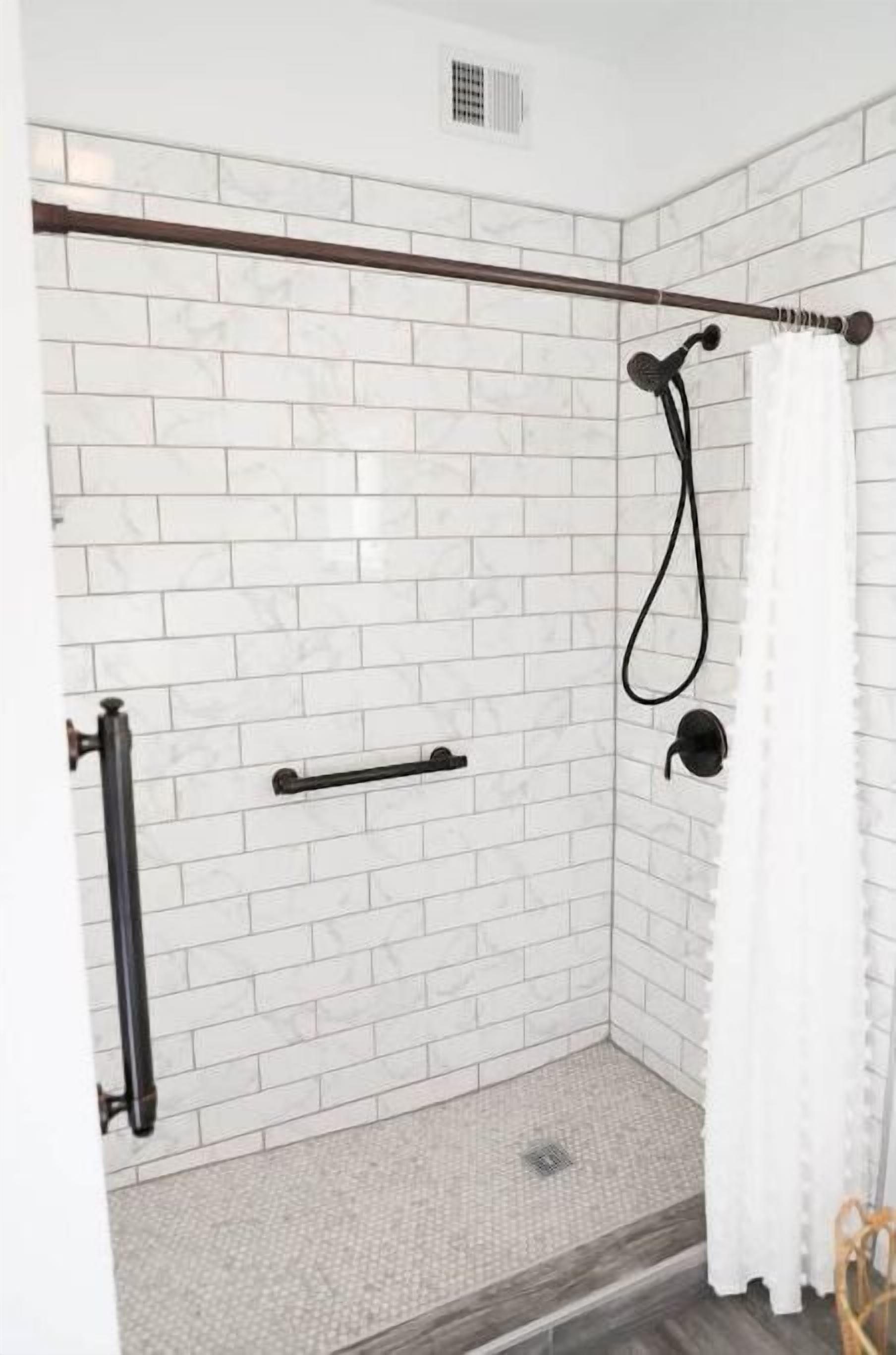 A shower area with white tiled walls, a wooden door frame, and a showerhead.