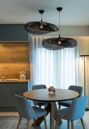 Uma cozinha moderna com uma mesa redonda de madeira, quatro cadeiras azuis e duas luminárias pendentes pretas.
