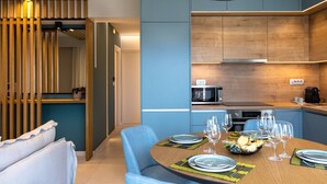 Un comedor moderno con una mesa redonda preparada para cuatro personas, una cocina con armarios de madera y una lámpara de techo original.