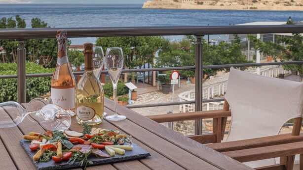 Una mesa con una botella de vino, copas y una tabla de embutidos en un balcón con vistas al mar.