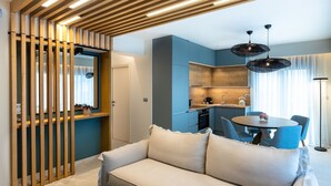 Una sala de estar moderna con sofá, una mesa de comedor con sillas, una zona de cocina y un techo con listones de madera e iluminación empotrada.