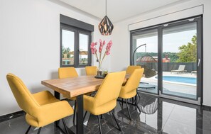 A dining area with a wooden table and yellow chairs, large windows with a view of a swimming pool and outdoor seating. - Luxurious home in Labin (Labin)