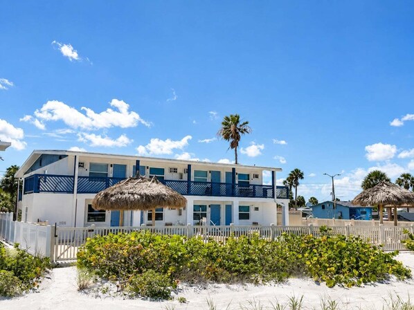 A two-story building with a white and blue exterior, a thatched roof, and a sandy beach in the foreground.