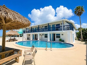 A two-story building with a swimming pool, a thatched umbrella, and a beach chair. - 🌊Chateau 3E - Beach front complex! Pool is Closed🌊 (Belleair Beach)