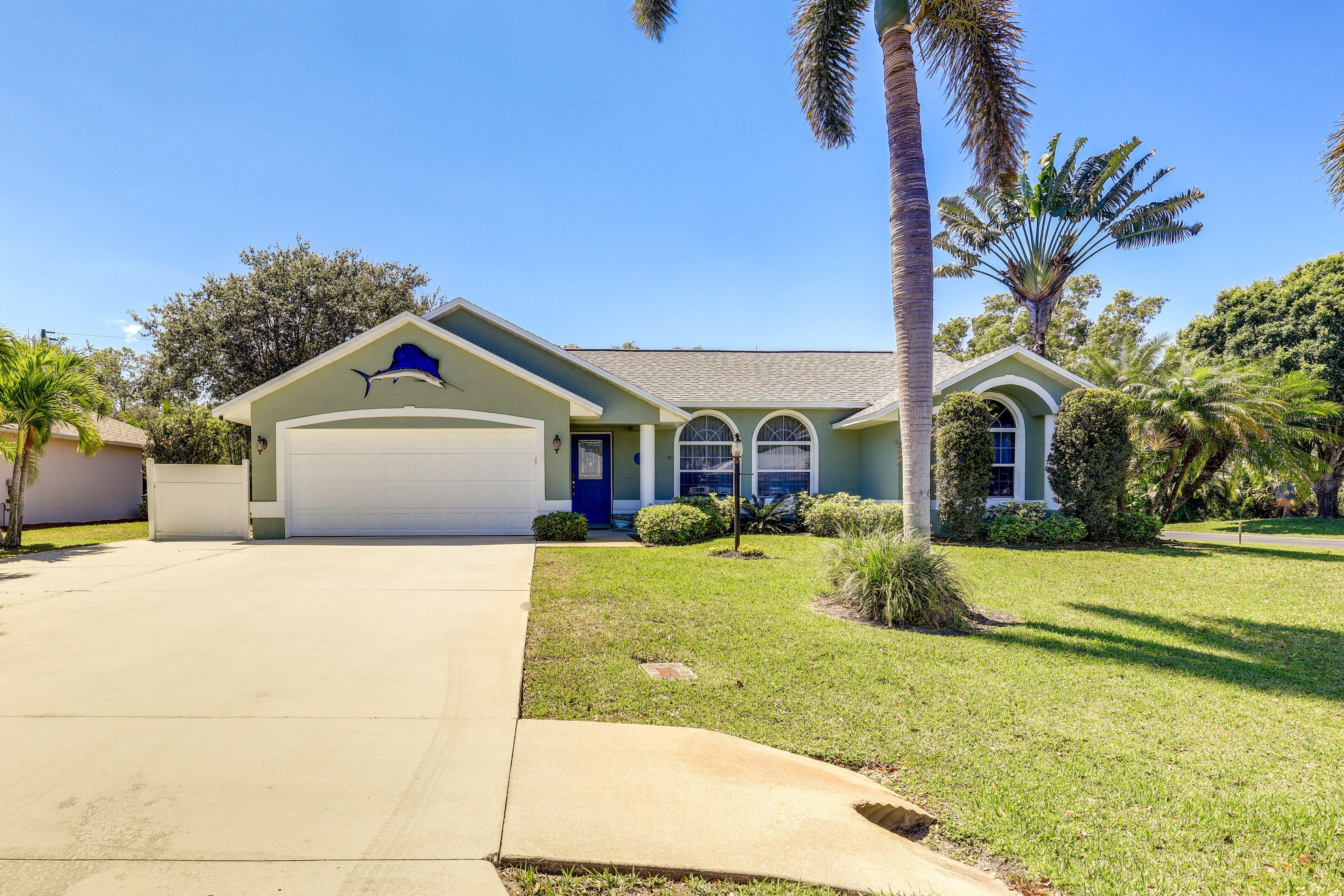 A single-story house with a garage, a front yard with grass and a palm tree, and a clear blue sky.