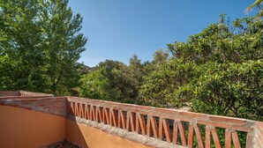 Un balcone con ringhiera in mattoni affacciato su un rigoglioso giardino con alberi e siepi di diverse varietà.