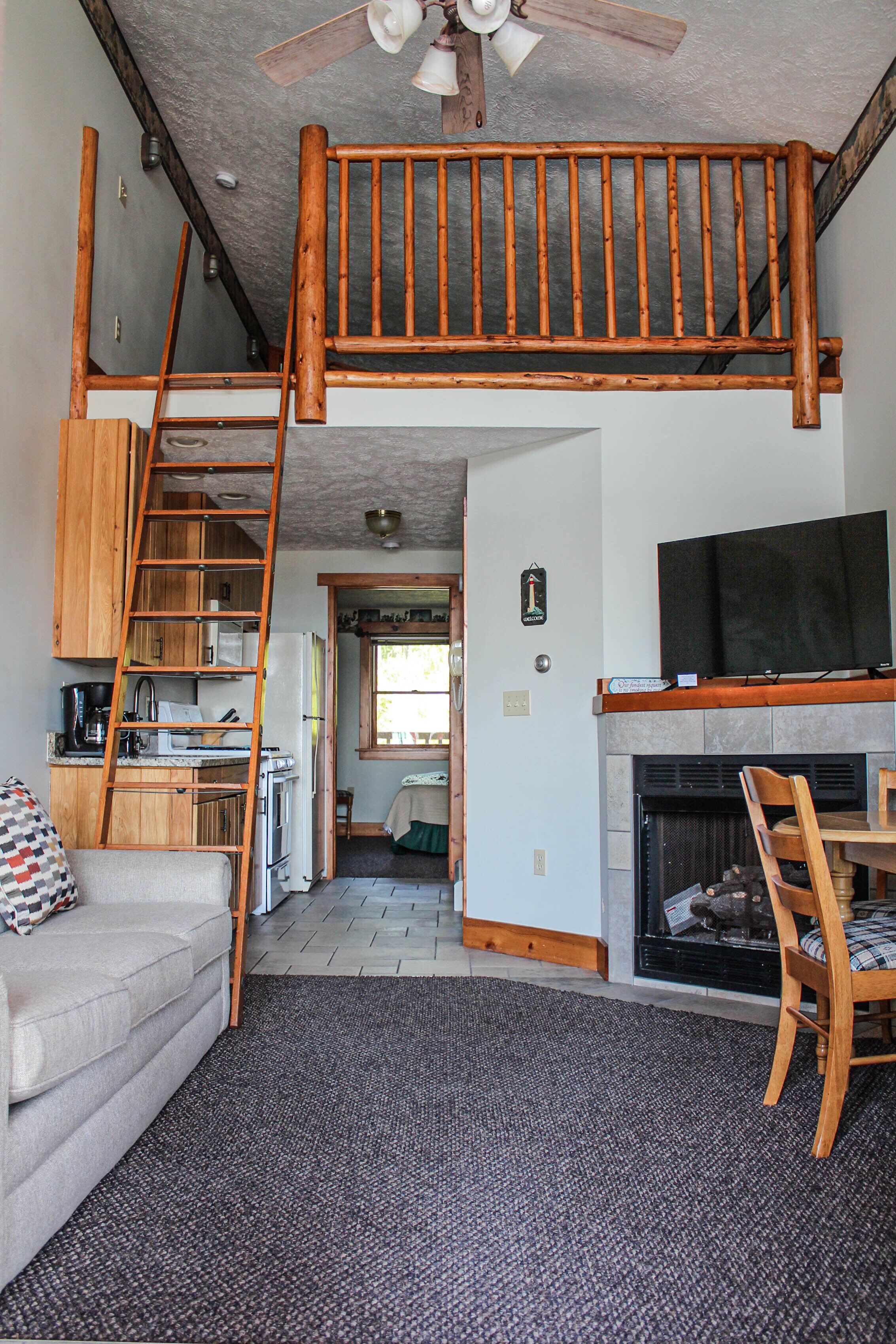 A loft-style living space with a wooden staircase, a kitchen area, a fireplace, and a television.