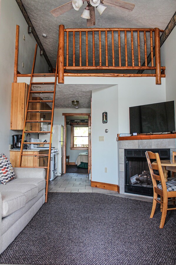 A loft-style living space with a wooden staircase, a kitchen area, a fireplace, and a television.