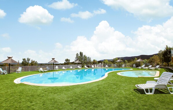 A swimming pool with two separate sections, surrounded by white lounge chairs and a well-maintained lawn.