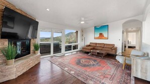 A spacious living room with a fireplace, a large window, a sofa, and a rug. - Walk to Uptown with Breathtaking Views and HotTub! (Sedona)