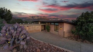 A building with a garage and a small patio area, surrounded by cacti and a mountainous landscape. - Walk to Uptown with Breathtaking Views and HotTub! (Sedona)