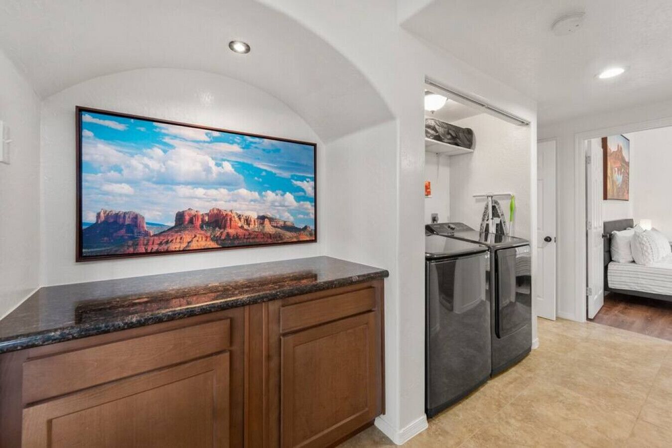 A kitchen with wooden cabinets, a granite countertop, a refrigerator, and a large landscape painting on the wall.