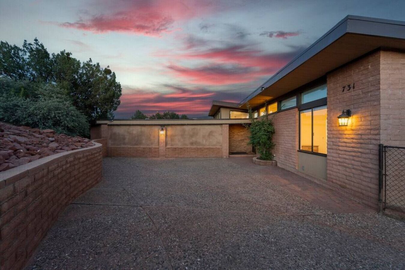 A modern building with a brick facade, numbered 731, featuring a gravel courtyard and a landscaped area with rocks and shrubs.