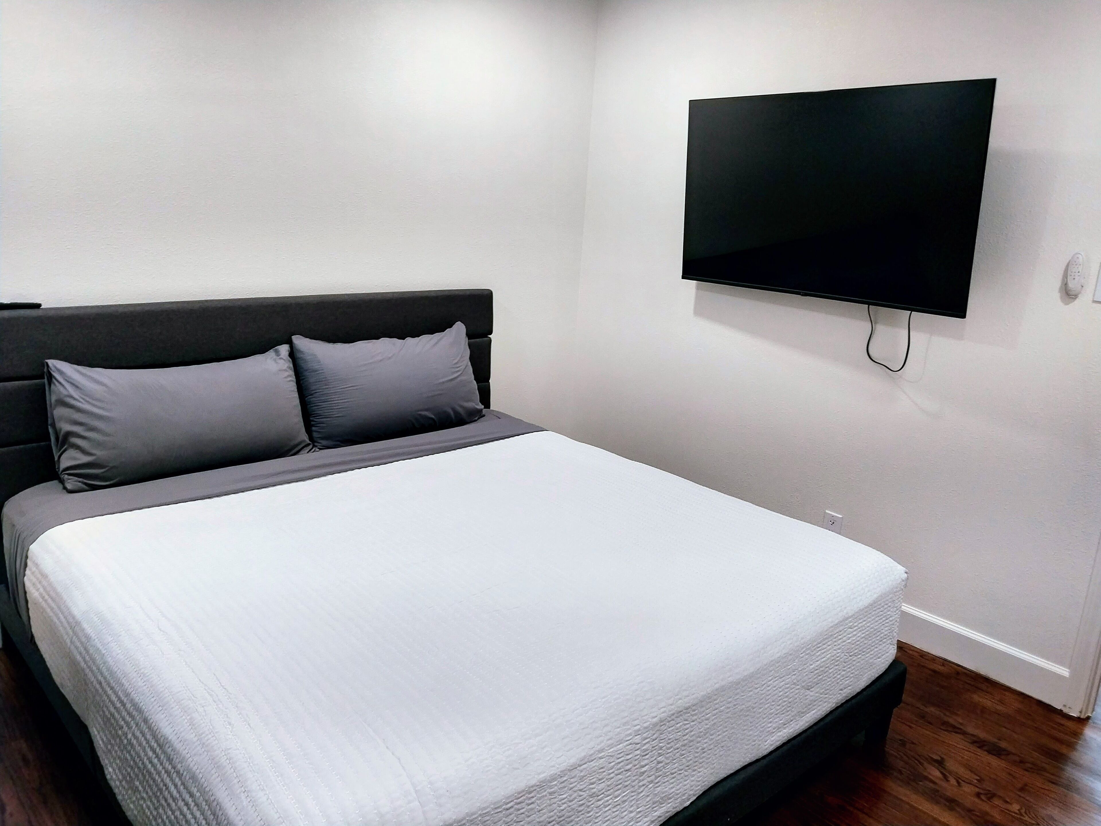 Een slaapkamer met een bed, twee kussens, een flatscreen televisie aan de wand en een houten vloer.