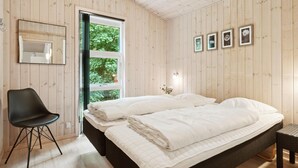 Un dormitorio con cama, una silla y ventana con vistas a follaje.