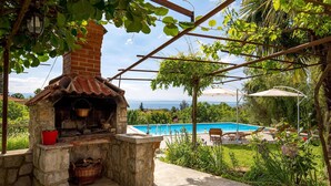 Eine Außenküche aus Stein mit Kamin, Pool und Meerblick.