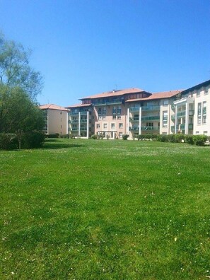 A multi-story building with a flat roof and large windows, surrounded by a well-maintained grassy area. - Charmant T2 Côte Basque (anglet)