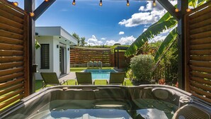 A hot tub area with a pool view, wooden pergola, and outdoor furniture.