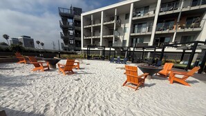 Ein Sitzbereich am Strand mit orangefarbenen Stühlen und einem Gebäude mit mehreren Balkonen im Hintergrund.