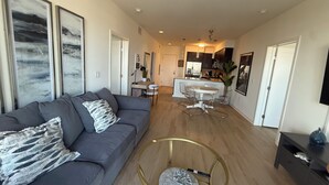 Ein modernes Wohnzimmer mit grauem Sofa, einem Couchtisch und einem Essbereich mit weißem Tisch und Stühlen.