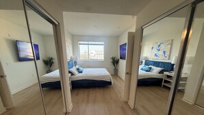Ein Schlafzimmer mit zwei Betten, einem Fenster, einem Gemälde und einer Pflanze.