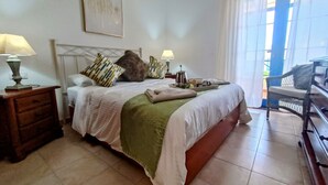 Una cama bien hecha con un edredón verde, dos lámparas de noche y una mesita de noche con lámpara.