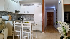 Una cocina moderna con armarios blancos, salpicadero de mármol y un comedor con mesa y sillas blancas.