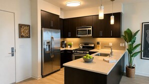 A modern kitchen with dark cabinetry, stainless steel appliances, and a central island with a bowl of green apples. - Marine Life: Smell the Sea, Feel the Breeze (Marina del Rey)