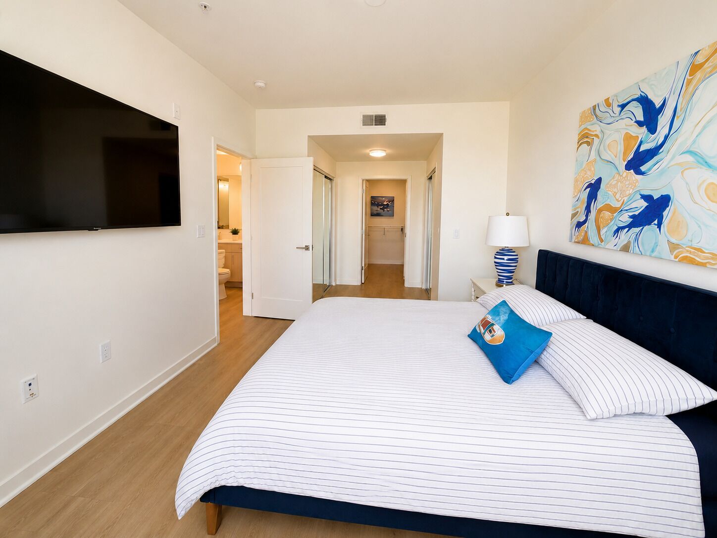 A hotel room with a bed, a TV, a painting, and a bathroom visible through an open door.